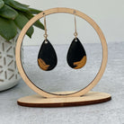 black and gold statement earrings hanging from a round display with plant in the background