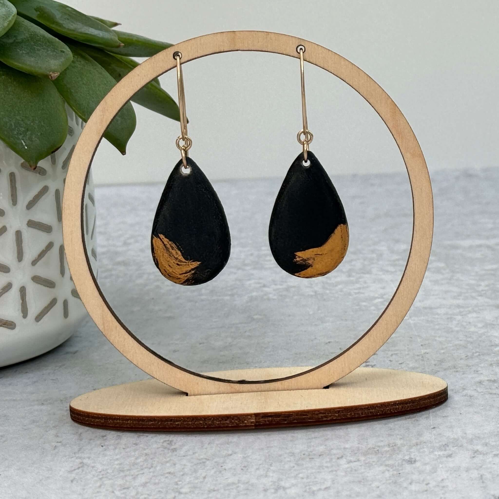 black and gold statement earrings hanging from a round display with plant in the background