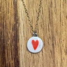 circular white necklace pendant with a red heart