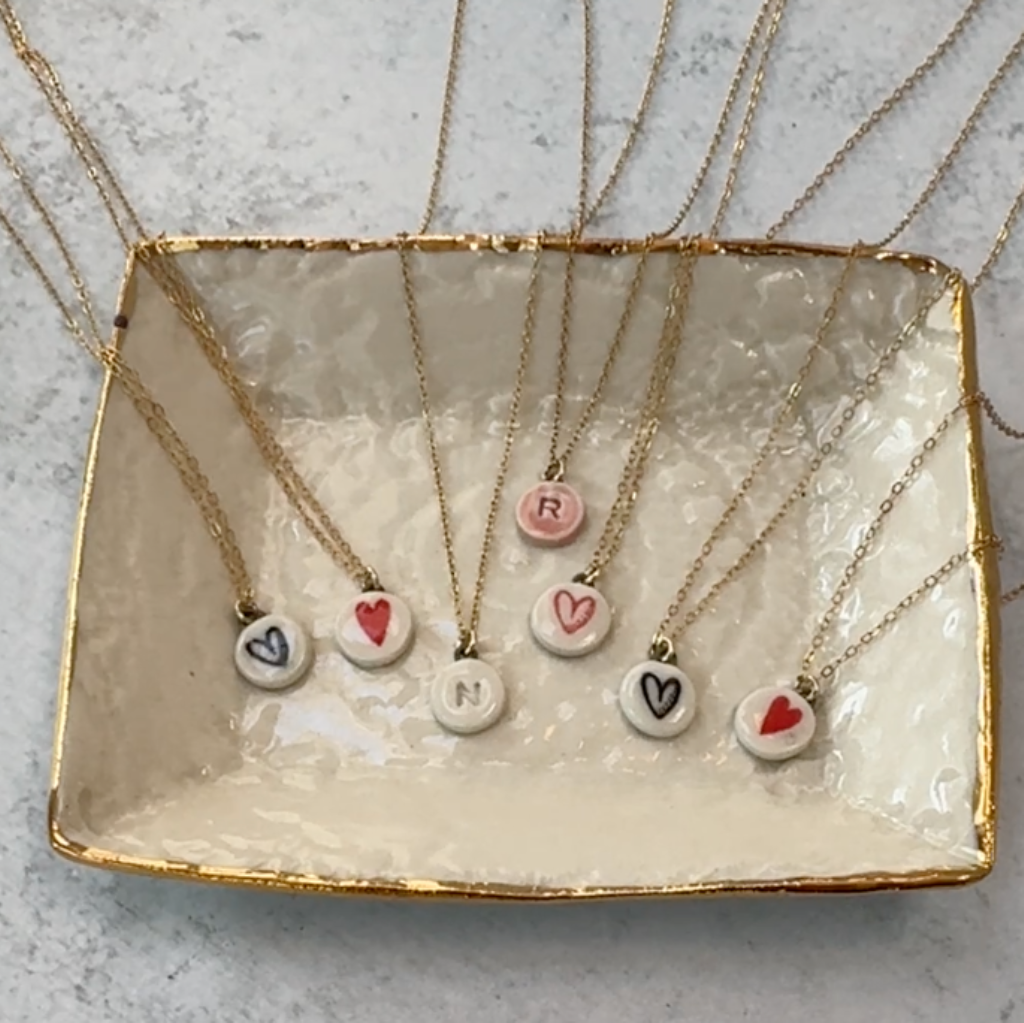 rectangular white dish with gold rim filled with 7 mini white heart necklaces 